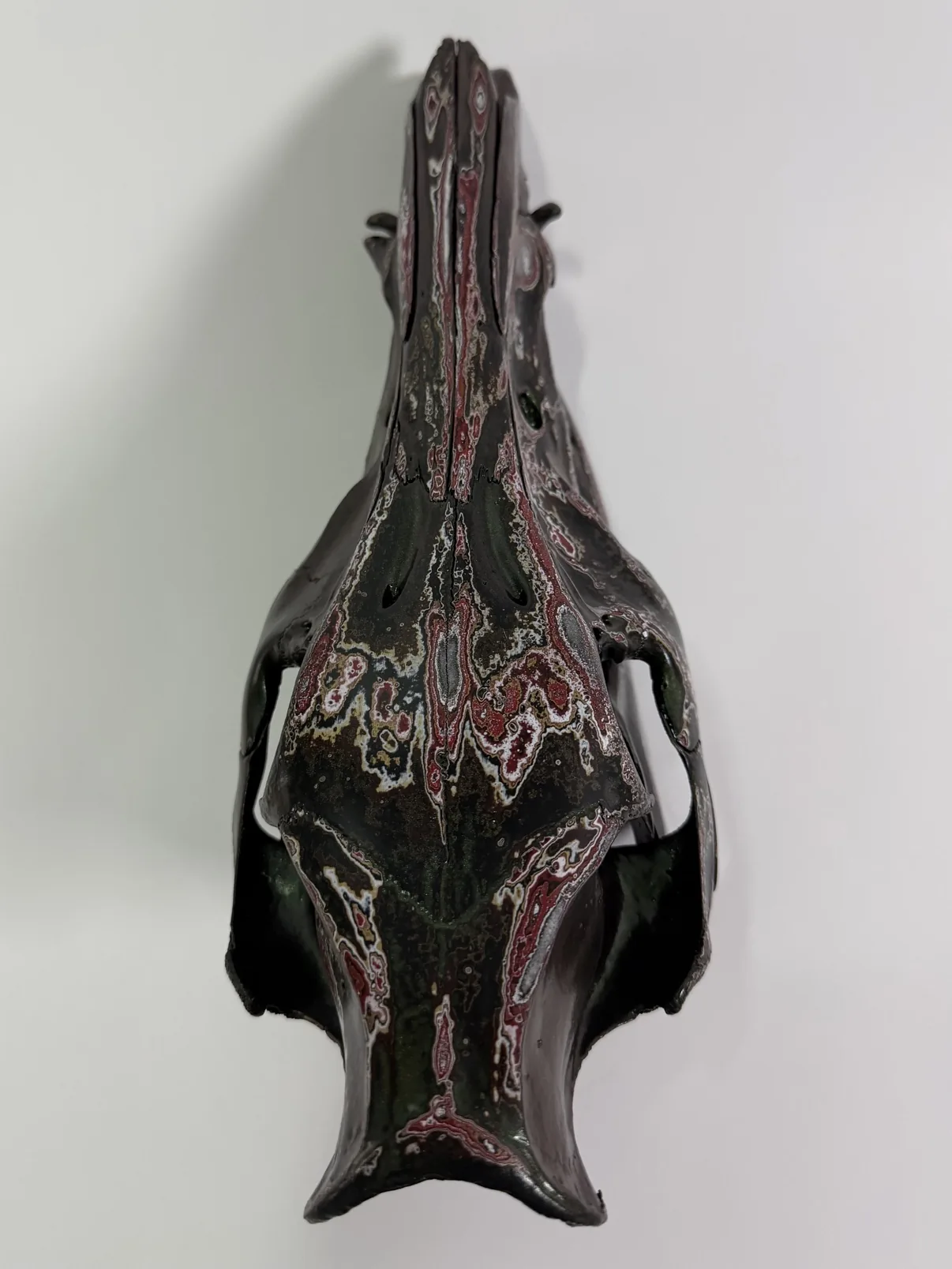 Photograph of the underside of my hand-painted feral hog skull, showing the metallic green palate and the fordite patterning along the jaw