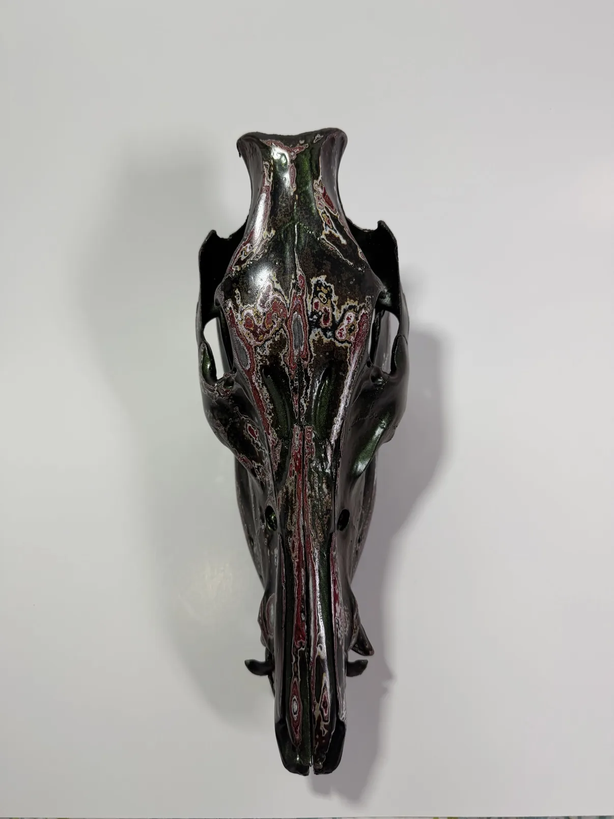 Photograph of my hand-painted feral hog skull from above, showing the burgundy and silver fordite pattern down the center of the skull