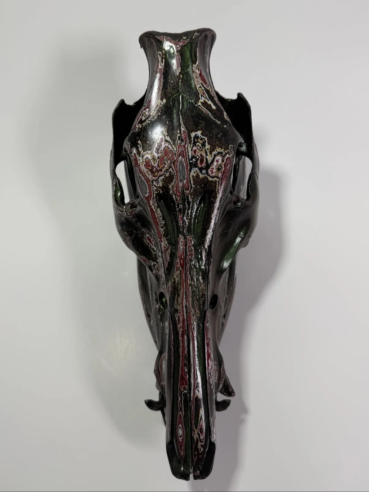 Photograph of my hand-painted feral hog skull from above and behind, showing the layered burgundy, black and green fordite finish