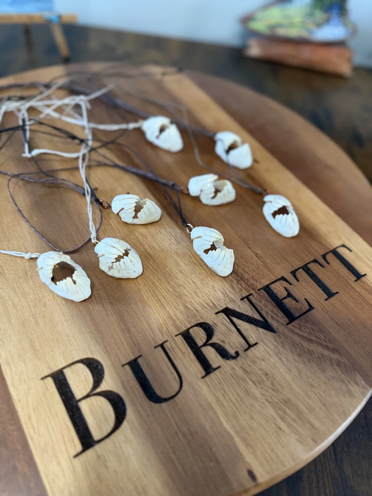 Photograph of my triggerfish jaw necklaces from an angled view on the round Burnett board, showing the white bone jaw pendants and their cords