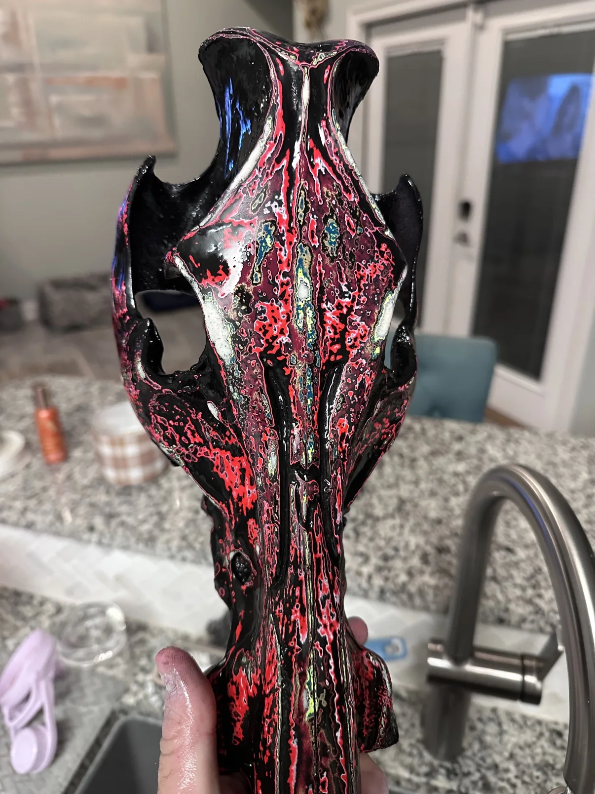 Photograph of my elongated hand-painted skull held in my hand, glossy black and red fordite finish